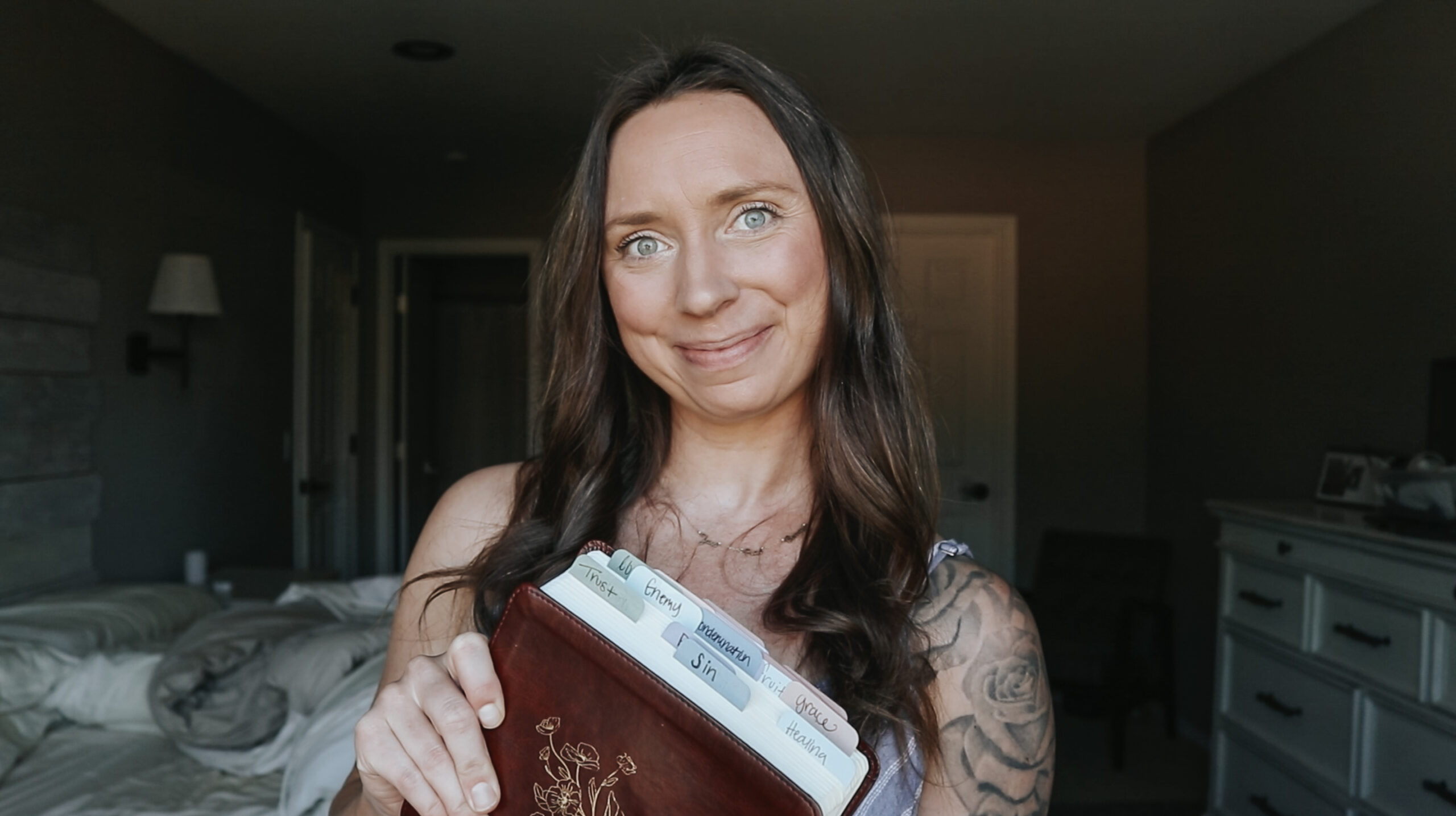 Christian homemaker smiles at the camera while holding up her bible that shows the tabs that organize her bible